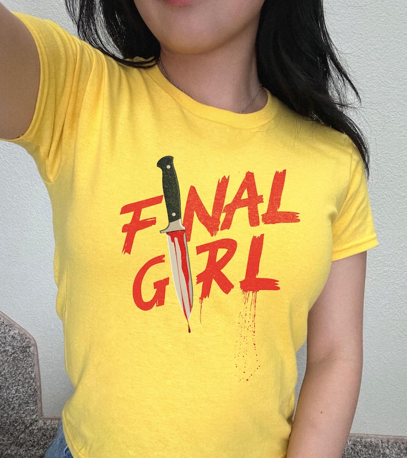 May include: Yellow t-shirt with the text "FINAL GIRL" in red with a bloody knife graphic.
