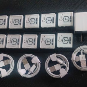 Puede incluir: Un conjunto de dispositivos electrónicos blancos, que incluyen pequeñas cajas cuadradas con el texto "ICE CURE" y un logotipo, un adaptador de corriente y varios cables USB blancos enrollados. Los artículos están dispuestos sobre una superficie oscura.