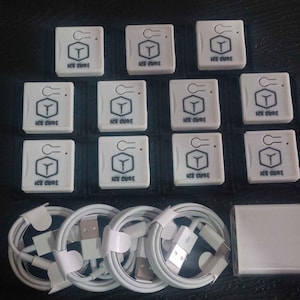 Puede incluir: Un surtido de dispositivos electrónicos y accesorios blancos. La imagen presenta múltiples dispositivos cuadrados pequeños con el texto "ICE CURE" y un gráfico, junto con varios cables de carga blancos y un adaptador de corriente.