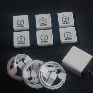 Puede incluir: Un conjunto de accesorios electrónicos blancos. La imagen muestra seis pequeñas cajas cuadradas con el texto "ICE CURE" y un logotipo, varios cables de carga blancos enrollados y un adaptador de corriente blanco, sobre una superficie oscura.