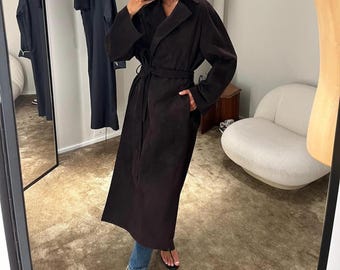 May include: A long, dark brown, belted trench coat with a lapel collar. The coat is made of a soft, smooth fabric and has a relaxed fit.