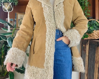 May include: A brown suede jacket with a white faux fur lining. The jacket has a collar and long sleeves. The jacket is worn by a person with blue jeans.