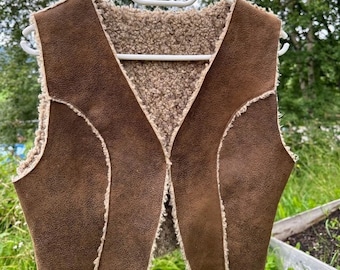 Op de afbeelding: Een bruin suède vest met een voering van imitatiebont. Het vest heeft een V-hals en is mouwloos.