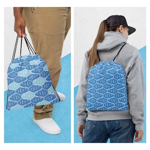 May include: A blue drawstring backpack with a repeating pattern of white fish. The bag is held by a person wearing khaki pants and white sneakers. Another person wears the backpack, showing the back view. The background is white and blue.