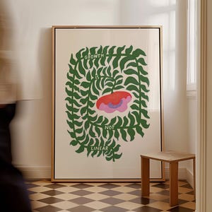 May include: A framed art print with the words "GROWTH IS NOT LINEAR" in green text. The artwork features a central red and pink floral design surrounded by green leaf-like shapes. A small wooden stool sits nearby.