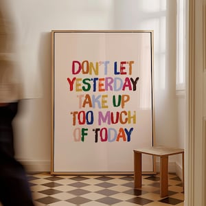 Könnte beinhalten: Ein gerahmter Kunstdruck mit dem Text "DON'T LET YESTERDAY TAKE UP TOO MUCH OF TODAY" in bunten Buchstaben. Das Kunstwerk wird in einem Raum mit einem kleinen Beistelltisch aus Holz und einem karierten Boden ausgestellt.
