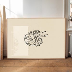 Puede incluir: Impresión enmarcada con un dibujo lineal negro de copas de cóctel en una bandeja. La frase "cin cin" está escrita en cursiva. La obra de arte está sobre un fondo crema, dentro de un marco de madera.