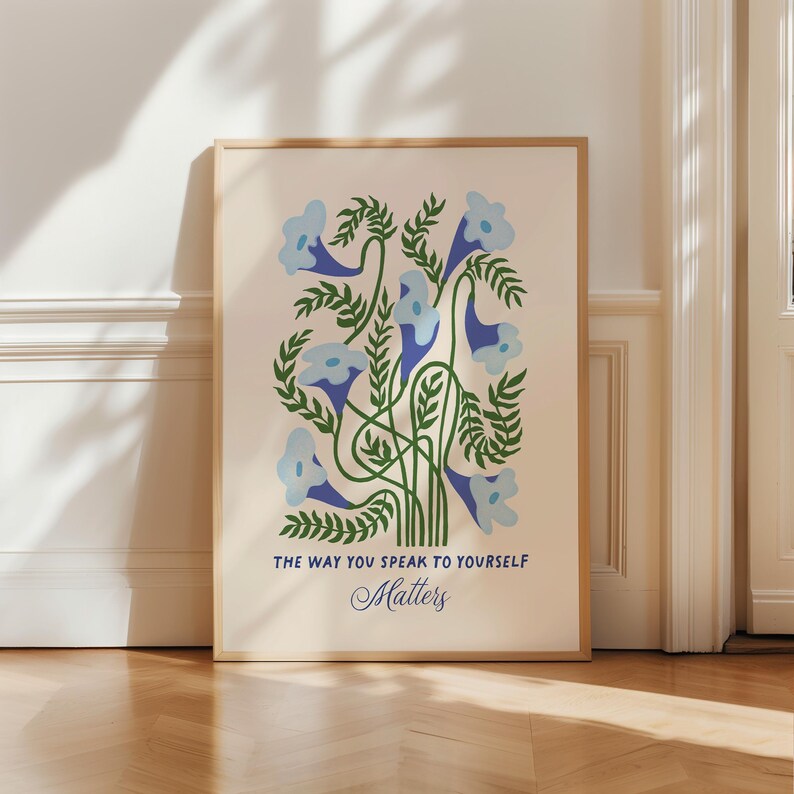 May include: A framed art print featuring a floral design with light blue flowers and green leaves. The artwork includes the text "THE WAY YOU SPEAK TO YOURSELF Matters" in blue and black font. The print is set against a cream background.
