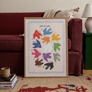 May include: A framed art print titled "MY COLORS" features colorful bird illustrations representing different hues. The birds are arranged in a circular pattern, with each bird labeled with a color name. The frame is a light brown color.