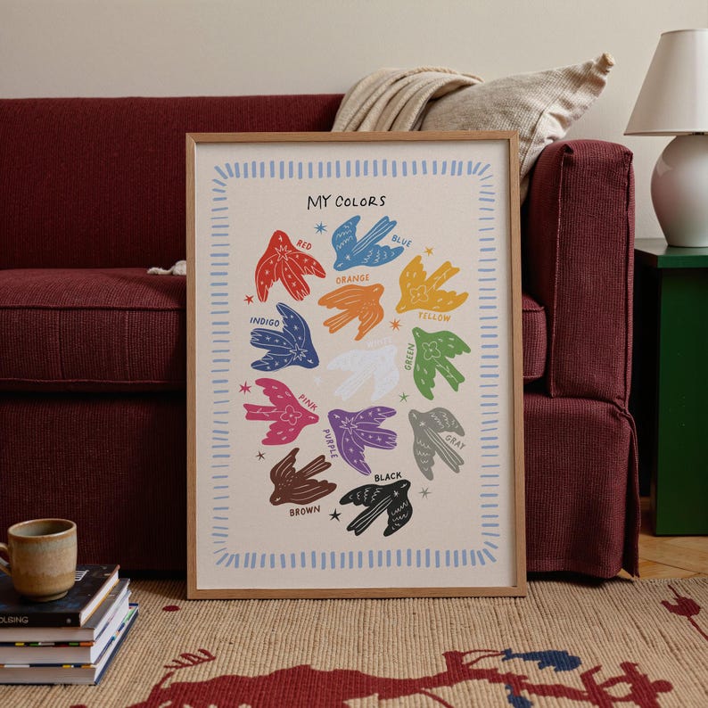 May include: A framed art print titled "MY COLORS" features colorful bird illustrations representing different hues. The birds are arranged in a circular pattern, with each bird labeled with a color name. The frame is a light brown color.