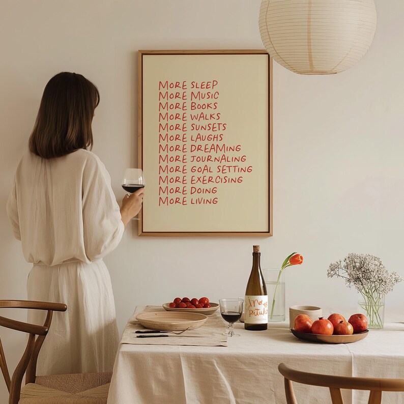 May include: A framed print with the text "More Sleep, More Music, More Books, More Walks, More Sunsets, More Laughs, More Dreaming, More Journaling, More Goal Setting, More Exercising, More Doing, More Living" in red lettering on a cream background.