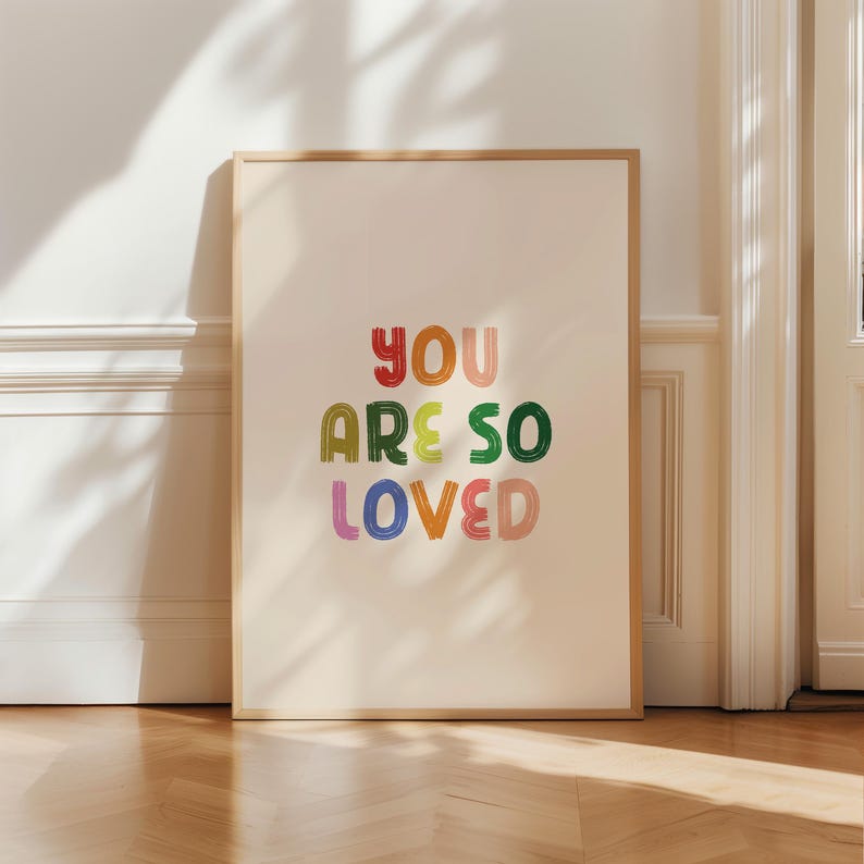 May include: A framed print with a white background and the text "YOU ARE SO LOVED" in colorful, handwritten letters.