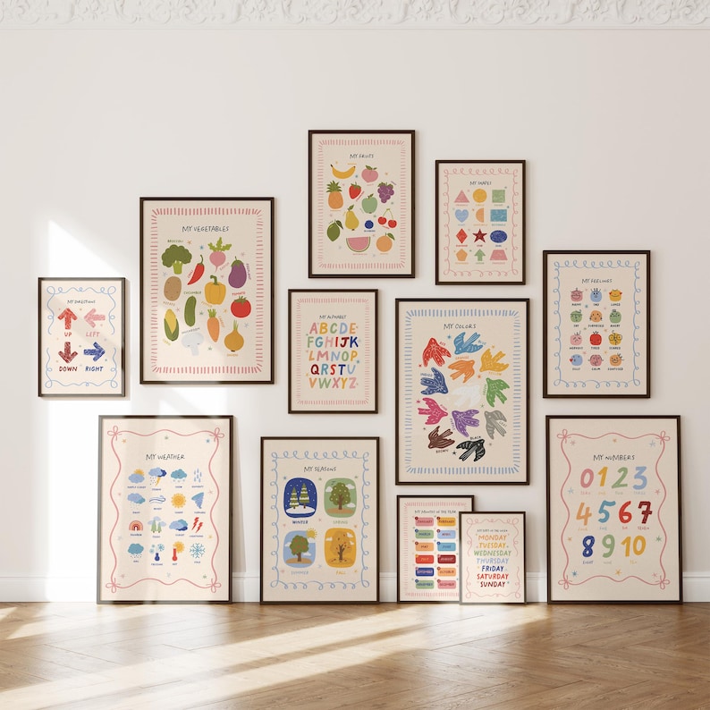 May include: A collection of framed educational posters with colorful illustrations. The posters cover topics like fruits, vegetables, shapes, colors, numbers, the alphabet, and the days of the week. Each poster has a decorative border and is displayed on a white wall.