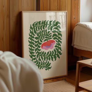 May include: A framed art print with the words "GROWTH IS NOT LINEAR" in a green leafy design. The artwork features a red and pink flower in the center, set against a cream-colored background. The frame is a light brown color.