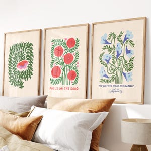 May include: Three framed art prints with botanical illustrations. One print features a green leafy design with a pink and red shape. The second print has red flowers and the text "FOCUS ON THE GOOD". The third print has blue flowers and the text "THE WAY YOU SPEAK TO YOURSELF Matters".