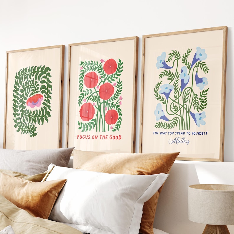 May include: Three framed art prints with botanical illustrations. One print features a green leafy design with a pink and red shape. The second print has red flowers and the text "FOCUS ON THE GOOD". The third print has blue flowers and the text "THE WAY YOU SPEAK TO YOURSELF Matters".