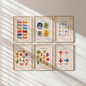 May include: Six framed educational posters with colorful illustrations. The posters cover topics like months, seasons, weather, fruits, vegetables, and directions. Each poster has a cream-colored background and a wooden frame.
