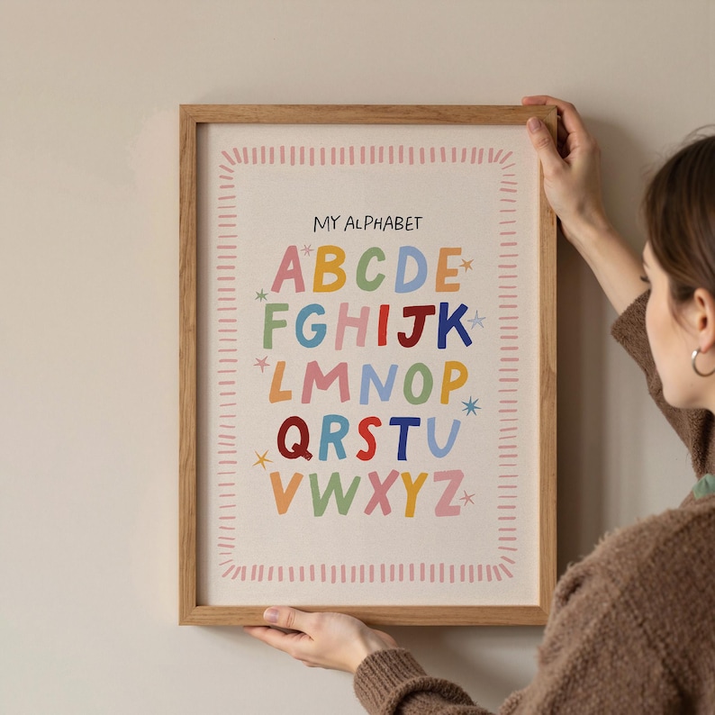 May include: A framed alphabet print with the text "MY ALPHABET" at the top. The colorful letters are arranged in rows, with star accents. The frame is a light brown color.
