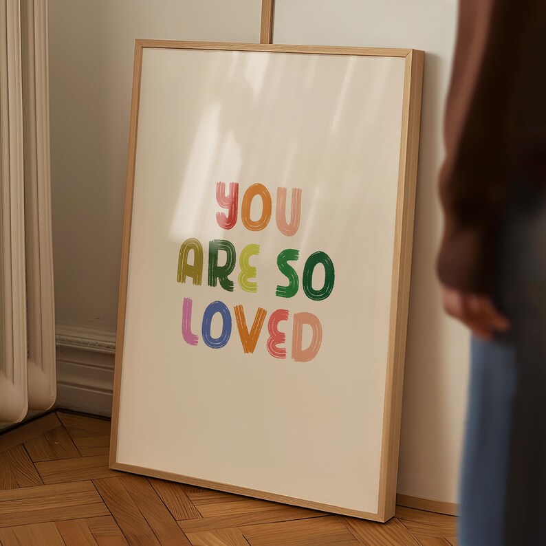 May include: A framed print with the text "You are so loved" in colorful, brushstroke-style lettering on a white background.