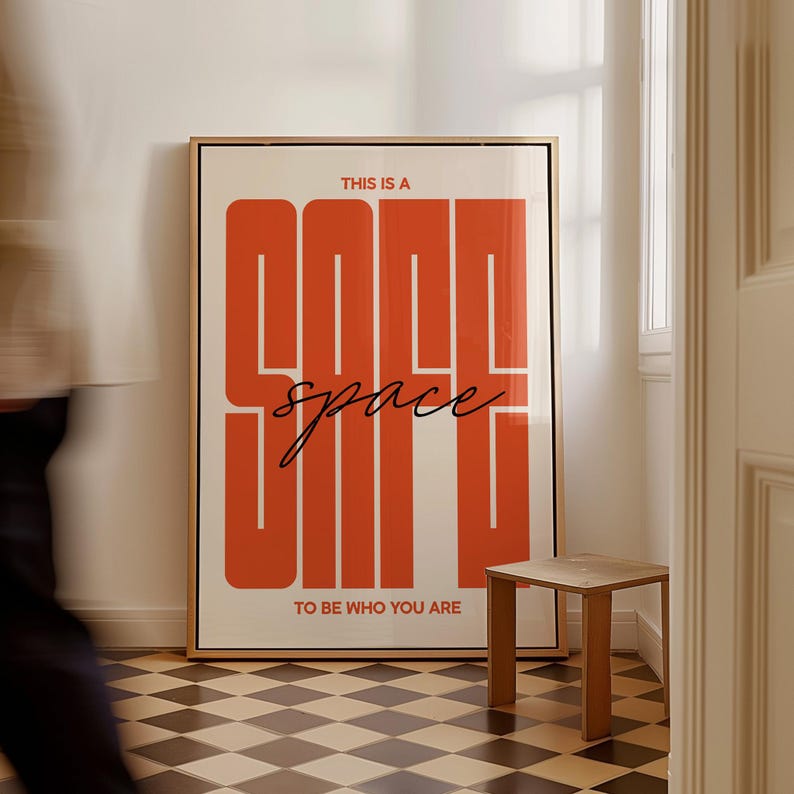 May include: A framed art print with the words "THIS IS A COOL SPACE" in large orange block letters, with "space" in cursive. The phrase "TO BE WHO YOU ARE" is below. The print is in a room with a small wooden table.