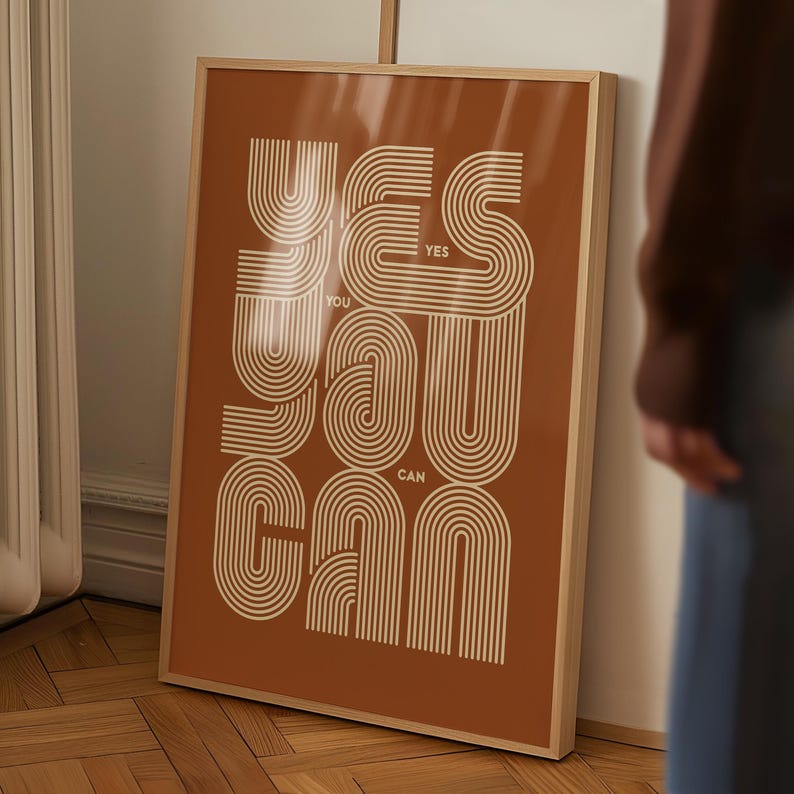 Pu&ograve; includere: Una stampa incorniciata con uno sfondo marrone e testo bianco che recita "YES YOU CAN" in uno stile di font retr&ograve; e sovrapposto.