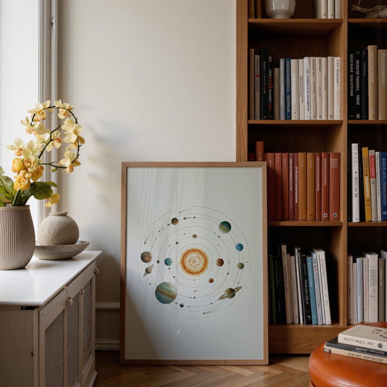 May include: A framed print of the solar system, featuring planets orbiting a central sun. The artwork has a light background and is displayed in a wooden frame. The print is placed near a window and a bookshelf.