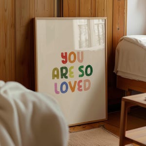 May include: A framed print with a cream background and the text "You are so loved" in colorful, stylized lettering.