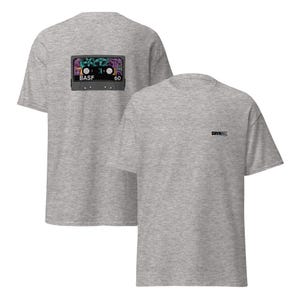 Puede incluir: Dos camisetas de color gris jaspeado. Una camiseta presenta un gr&aacute;fico de cinta de cassette colorida en la parte posterior con el texto "BASF 60". La otra camiseta tiene el texto "DRVN" impreso en la parte delantera.