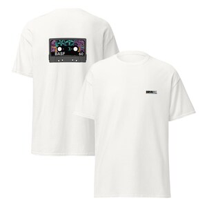 Puede incluir: Dos camisetas blancas. Una camiseta tiene un gr&aacute;fico de cinta de cassette colorido en la parte posterior con el texto "BASF 60". La otra camiseta tiene el texto "DRVN" en la parte delantera.
