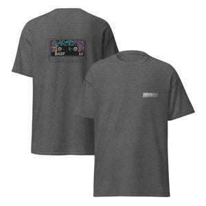 Puede incluir: Camisetas grises oscuras con un dise&ntilde;o de cinta de cassette en la espalda, con detalles coloridos y el texto "BASF 60". En la parte delantera, el texto "DRVN VHS".