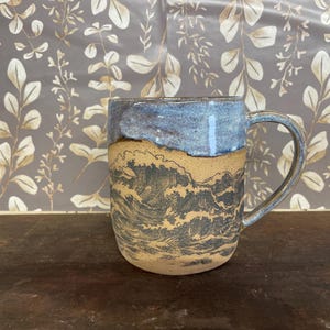 May include: A ceramic mug with a blue glaze and a brown base. The mug has a wave design in black and white.