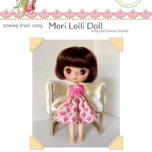 Peut inclure: Une poupée aux cheveux bruns et aux grands yeux portant une robe sans manches rose avec un motif de pastèque. La poupée est assise sur une petite chaise en bois. L'image comprend le texte "Little Noel" et "Mori Lolli Doll".