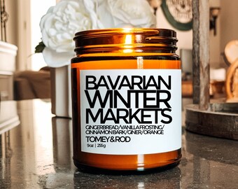 May include: A brown glass jar candle with a white label that reads "Bavarian Winter Markets." The candle's scent includes gingerbread, vanilla frosting, cinnamon bark, ginger, and orange. The candle is 9 oz (255g).