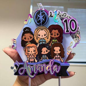 May include: A vibrant cake topper with six cartoon characters, each with different hair and clothing. The topper displays the name "Amanda" in cursive, musical notes, and the number "10". The design has a holographic finish.