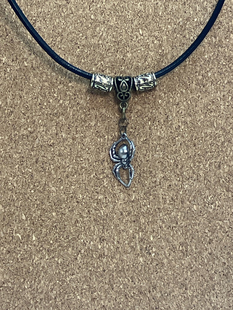 May include: A black leather necklace with silver and bronze beads and a silver spider pendant.