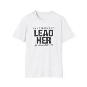 Peut inclure: T-shirt blanc avec l'inscription "MY ASSIGNMENT: LEAD HER EPHESIANS 5:23" en noir vieilli. Le t-shirt a des manches courtes et un col rond.