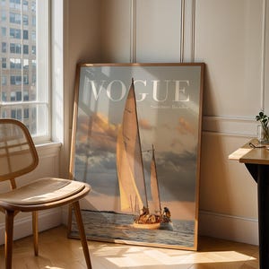 May include: A large framed wall art print featuring a sailboat on the water at sunset with the word VOGUE and the text Summer Reader printed in white at the top. The image depicts a sailboat with tan sails against a cloudy sky and calm sea.