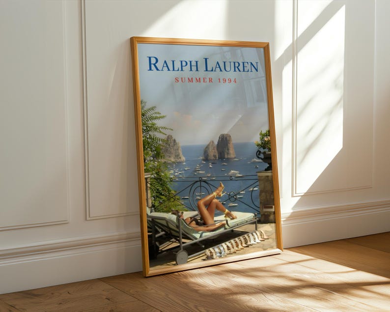 May include: A framed poster featuring the text RALPH LAUREN SUMMER 1994. The image depicts a person reclining on a lounge chair on a balcony overlooking a blue sea with rocky islands and boats. A row of sandals is lined up on the floor nearby.