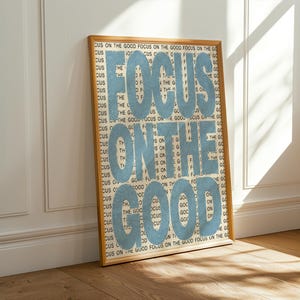 May include: A framed rectangular wall art print featuring the repeating black text FOCUS ON THE GOOD in the background, overlaid with the large, bold, light blue text FOCUS ON THE GOOD centred across the entire surface of the print.