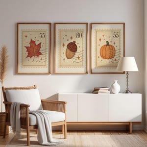 May include: Three framed wall art prints designed as vintage postage stamps. The left print features a red maple leaf, the center an acorn, and the right a pumpkin. Each includes numerical values 55 or 80, star accents, and wavy postmark lines.
