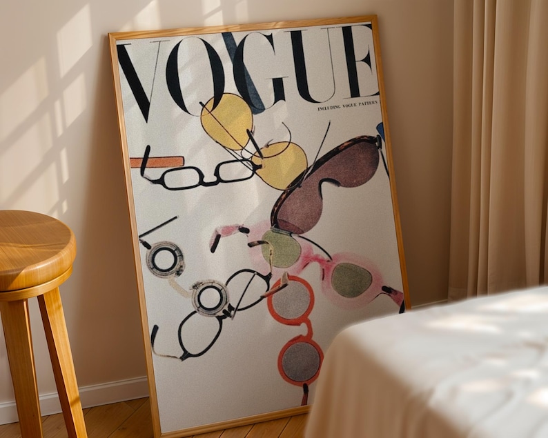 May include: A framed wall art print featuring the word VOGUE in large black letters at the top. The design displays a scattered collection of various eyeglasses and sunglasses in shades of yellow, brown, pink, and orange against a white background.