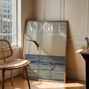 Op de afbeelding: Een grote ingelijste wandposter met een tijdschriftomslagontwerp met de tekst VOGUE, Summer Reader en Beauty and Lifestyle. De afbeelding toont een persoon die in de oceaan duikt met het zeeoppervlak zichtbaar onder de horizonlijn.