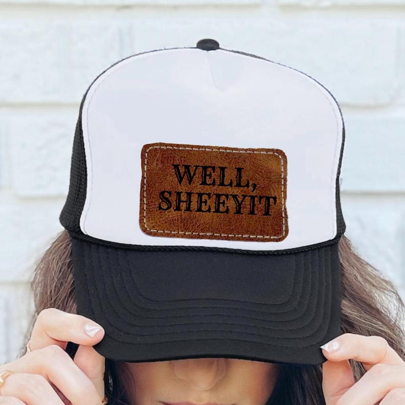 May include: A white and black trucker hat with a brown leather patch that says "WELL, SHEEYIT".