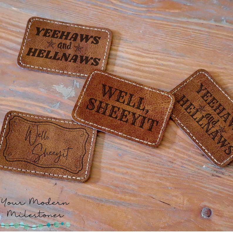 May include: Four brown leather coasters with white stitching. The coasters have different sayings on them, including "Yeehaws and Hellnaws", "Well, Sheeyit", and "Well, Sheeyit".