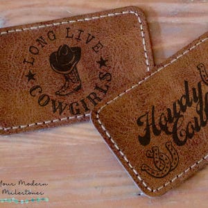 May include: Two brown leather patches with stitched edges. One patch has the text "Long Live Cowgirls" with a star on each side and a drawing of a cowboy hat and boot. The other patch has the text "Howdy Cowgirl" with two horseshoe shapes.