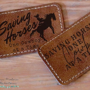 May include: Two brown leather patches with stitched edges. The top patch features a silhouette of a cowgirl riding a horse with the text "Saving Horses One Cowboy at a Time". The bottom patch features the text "Saving Horses One Cowboy at a Time".