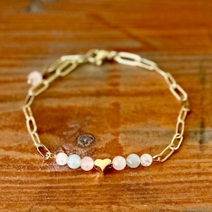 May include: A gold chain bracelet with a heart charm and alternating light blue and pink beads.