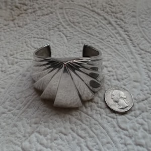 May include: A silver bracelet with a fan-shaped design. The bracelet is about the size of a quarter.