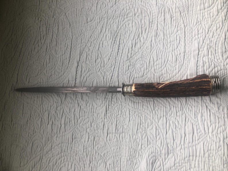 May include: A knife with a long, slender, silver blade and a handle made of brown antler material. The handle is secured with silver metal rings. The knife is designed for cutting and slicing.