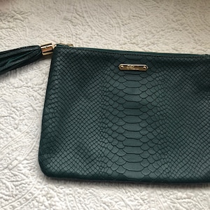 May include: A dark green snakeskin-embossed clutch with a gold zipper and a matching tassel.